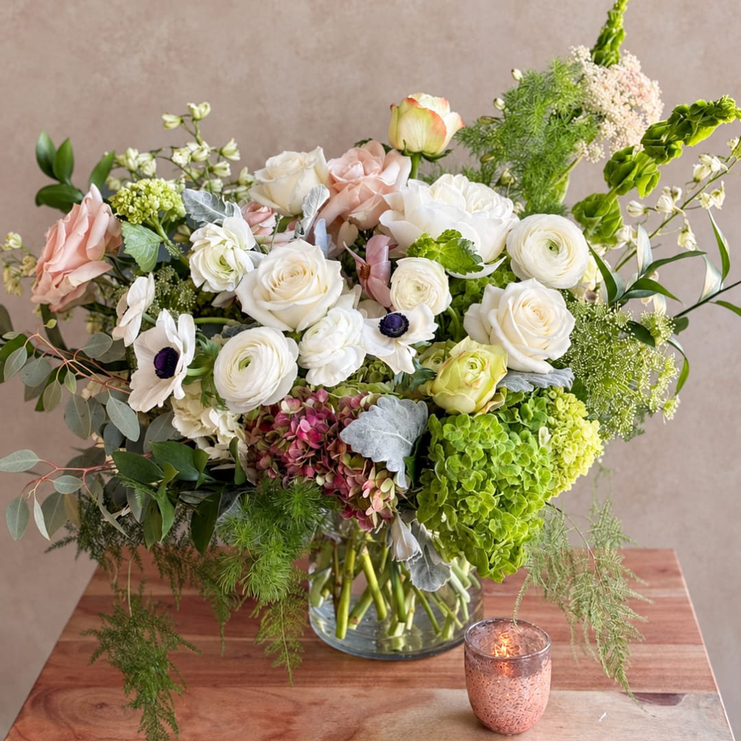 Large mixed bouquet of white, blush, and green flowers in a glass vase