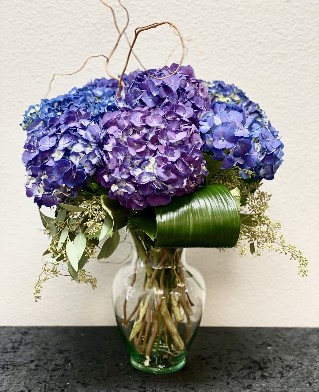 Purple hydrangea bouquet in a glass vase with curly branches