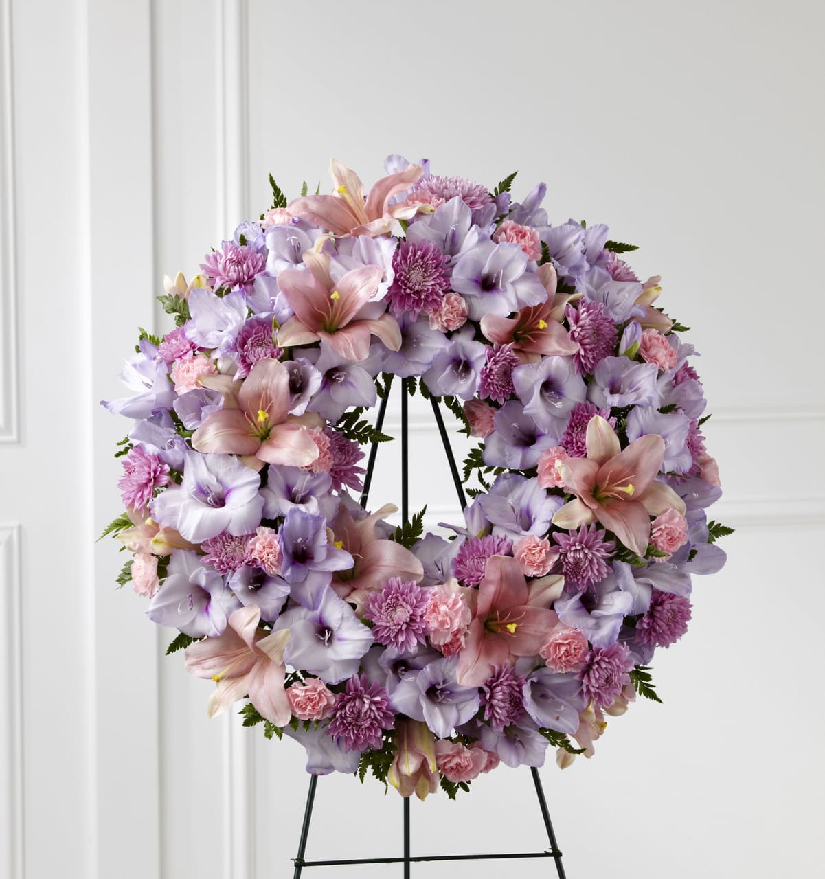Large wreath of lavender and pink lilies, carnations, and mums on a metal easel stand