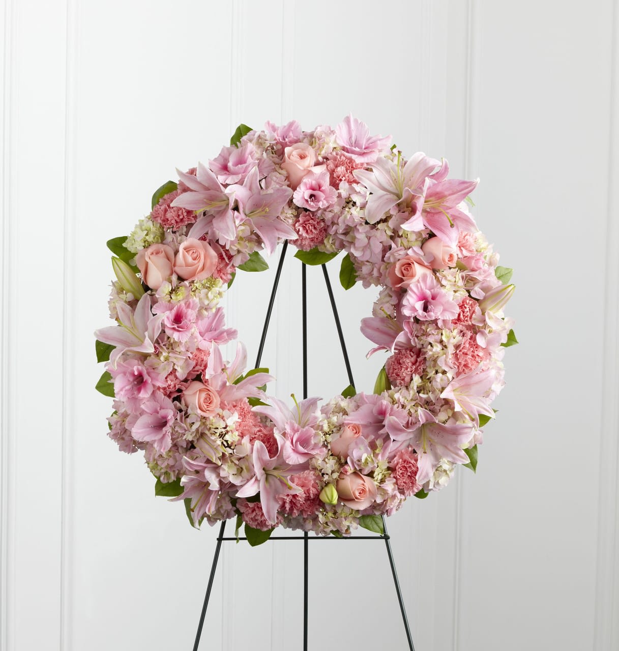 Pink floral wreath with lilies, roses, and carnations on a metal easel