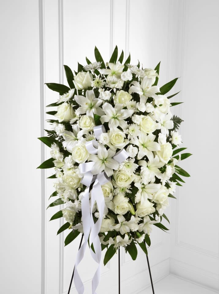 Oval white standing spray with lilies, roses, and carnations on an easel stand.