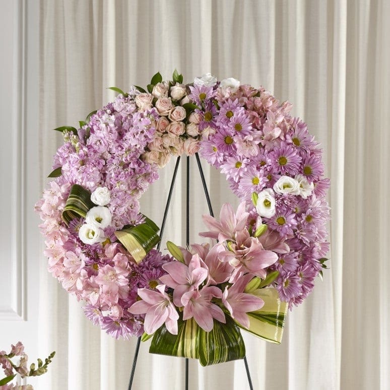 Large pink floral wreath with lilies, roses, and mums on a black metal stand