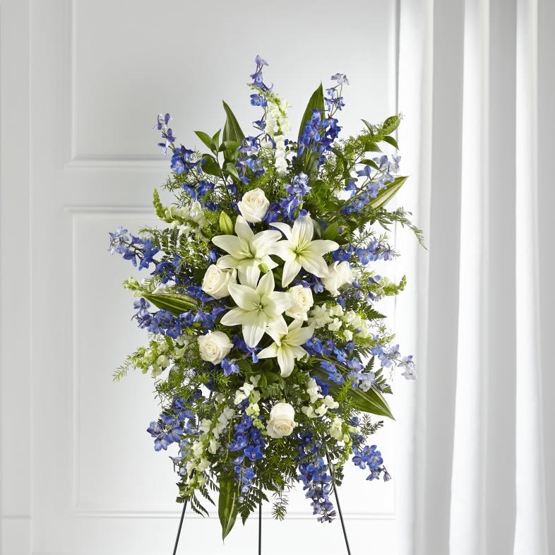 Tall standing floral spray with white lilies, white roses, and blue flowers