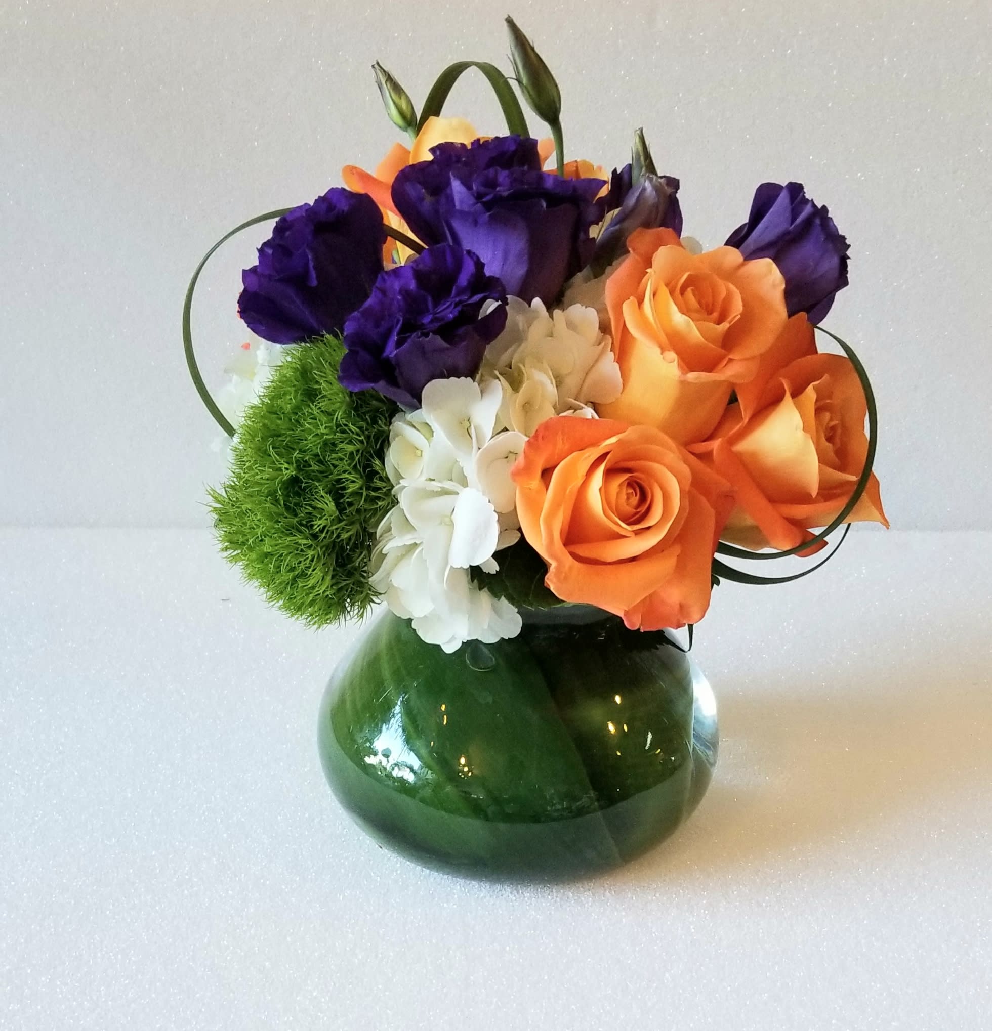 Bouquet of orange roses and purple lisianthus in a green glass vase