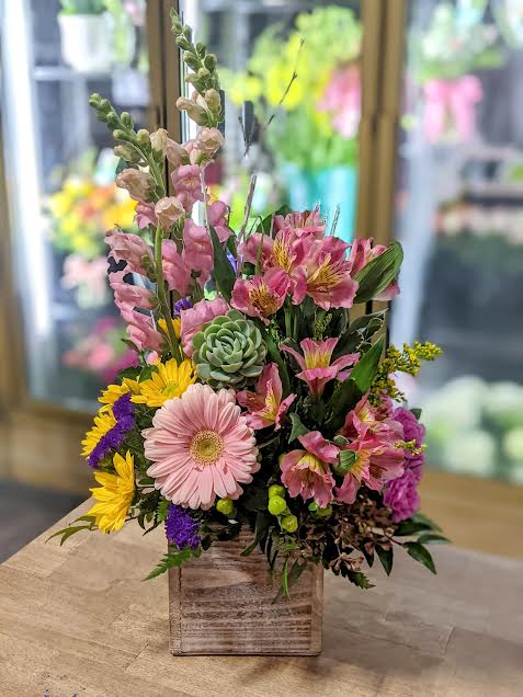 Mixed floral arrangement in a wooden box with pink and yellow blooms