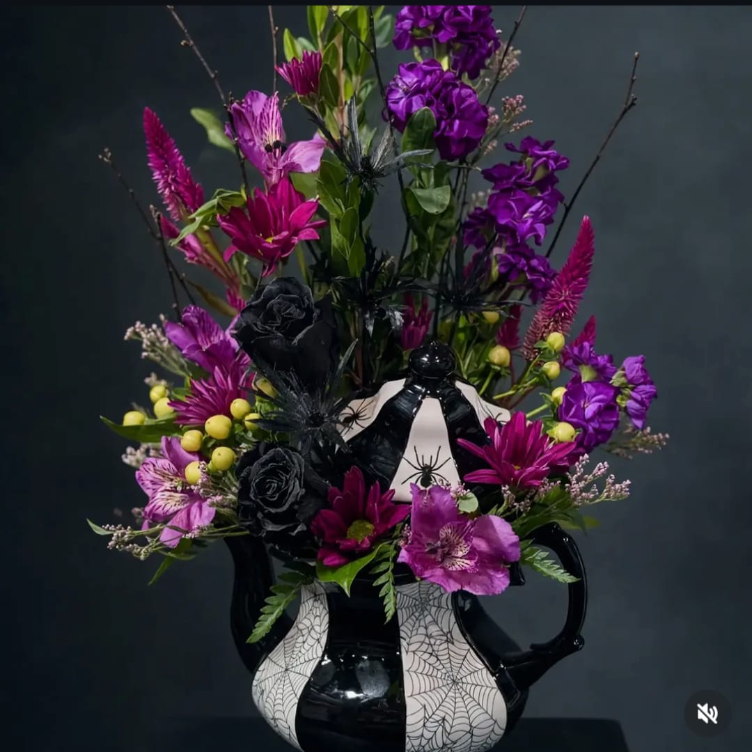 Purple floral arrangement in a black-and-white spiderweb vase with Halloween accents