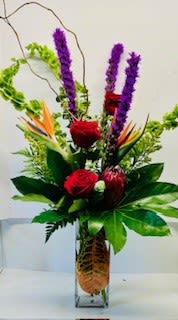 Tropical flower arrangement with red roses and purple spikes in a glass vase