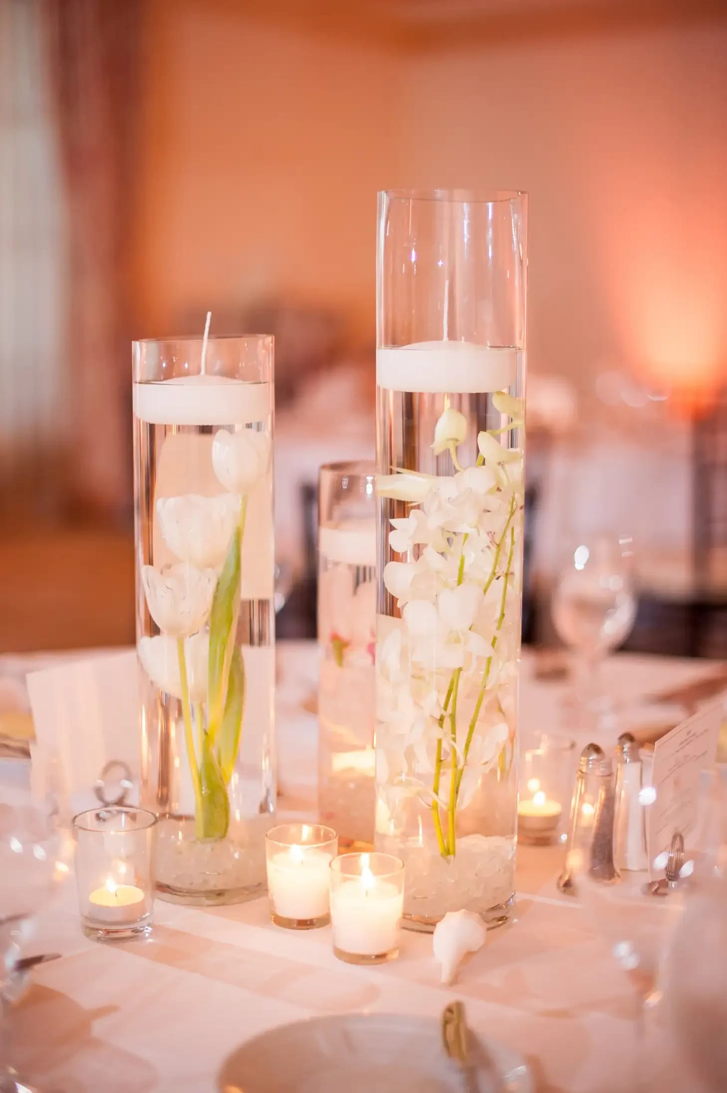 Tall glass vases with white flowers and floating candles on a table