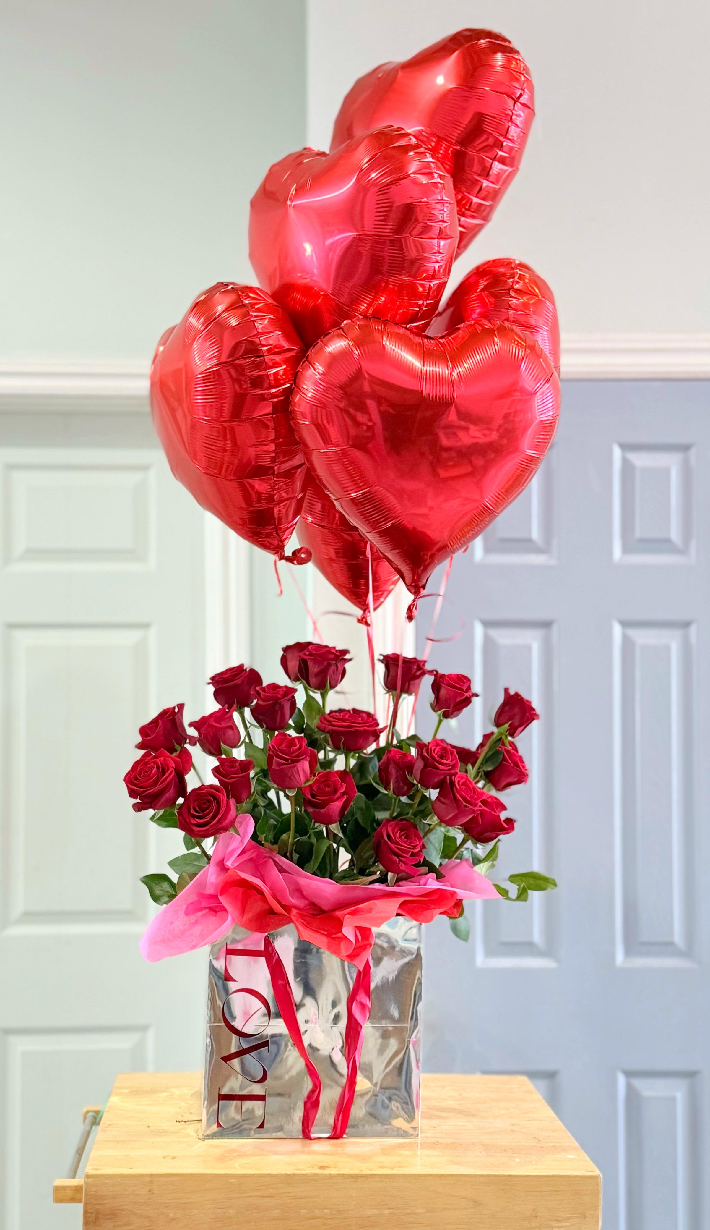 Red roses in a silver gift bag with red heart balloons