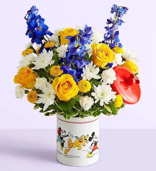 Bouquet of yellow roses, white daisies, and blue flowers in a Mickey Mouse tin