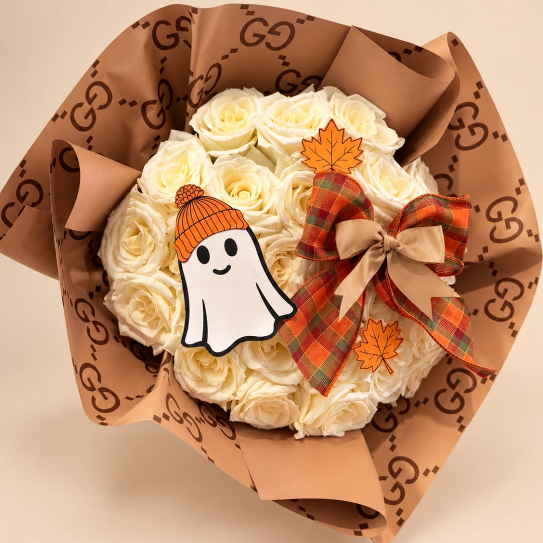 Bouquet of cream roses wrapped in brown paper with a plaid bow and Halloween decorations