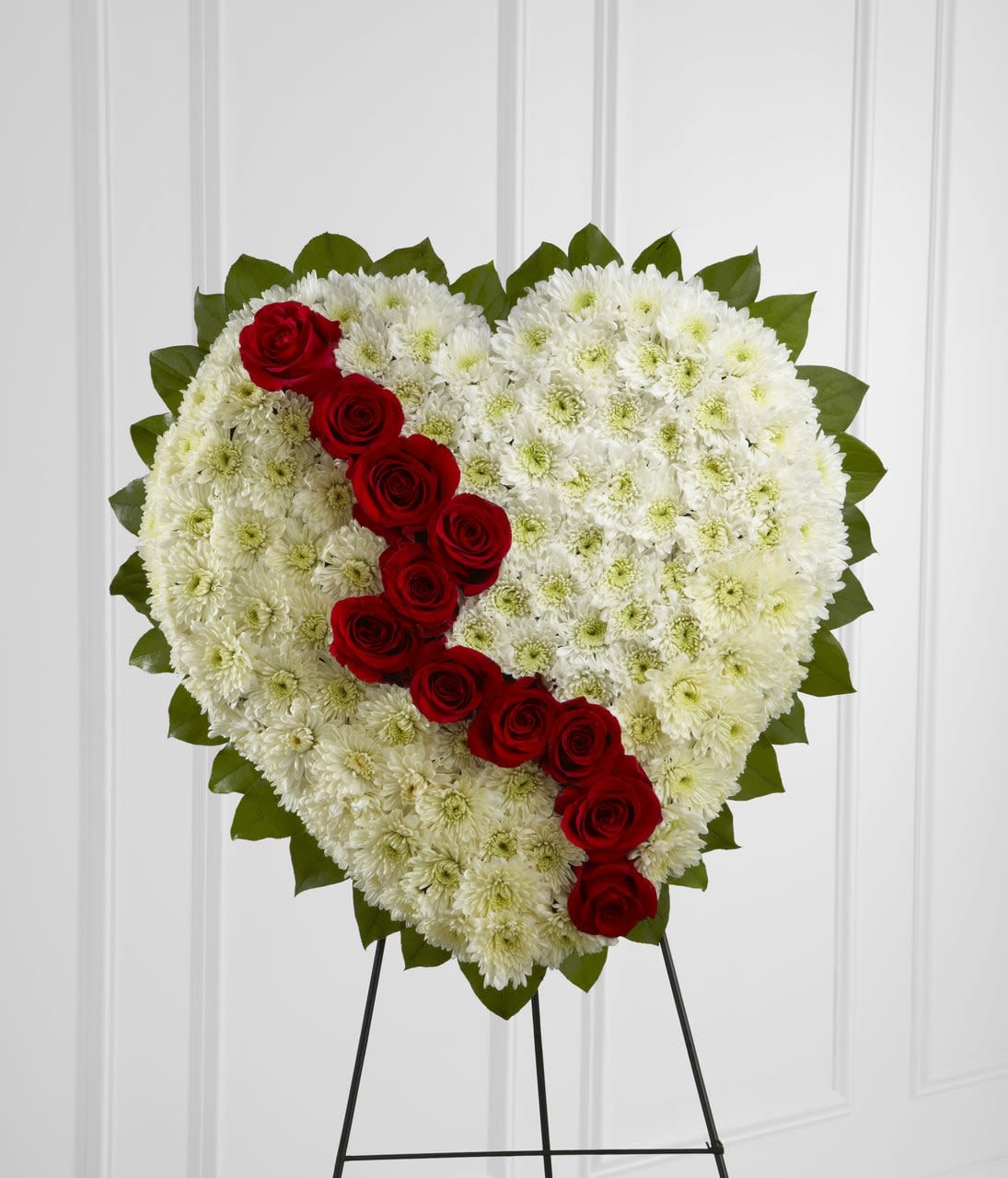 TLSP The Broken Heart - The Broken Heart is a beautiful way to express the impact that the departed had on your life. Pearly white chrysanthemums form the shape of a heart, accented with greens lined around the oustide and "broken" in the middle with a line of rich red roses to create an exquisite way to honor the life of the deceased at their memorial service. Displayed on a wire easel. Approximately 22"H x 22"W.  Your purchase includes a complimentary personalized gift message.