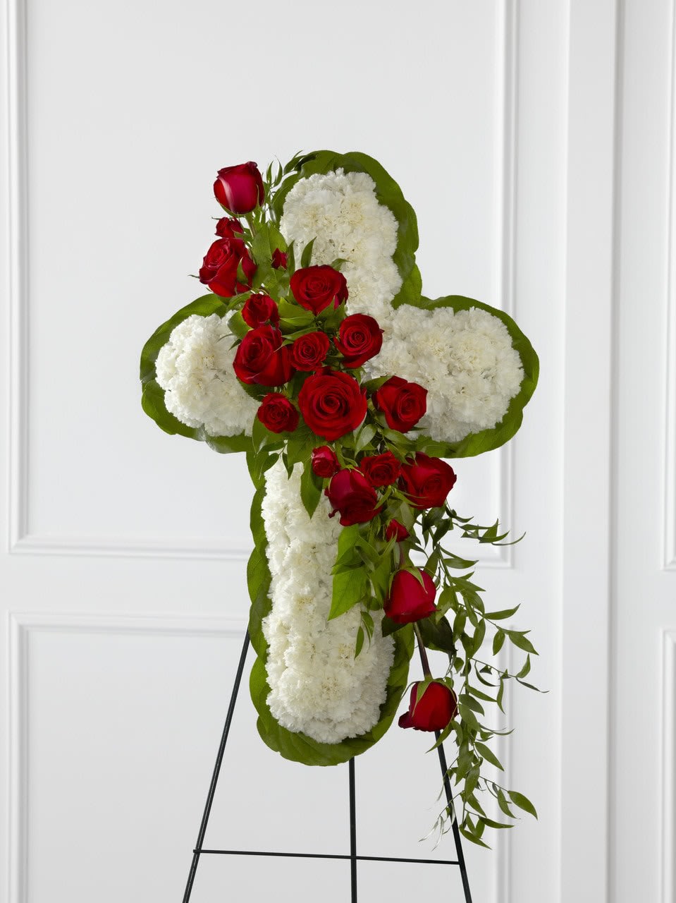 TLSP The Floral Cross Easel - The Floral Cross Easel is a symbol of love and faith to honor the deceased at the final farewell service. White carnations are arranged to form a cross in which an accent of red roses, spray roses, and lush greens are draped across the center, creating a beautiful display of serene elegance. Displayed on a wire easel. Approximately 38"H x 24"W.  Your purchase includes a complimentary personalized gift message.