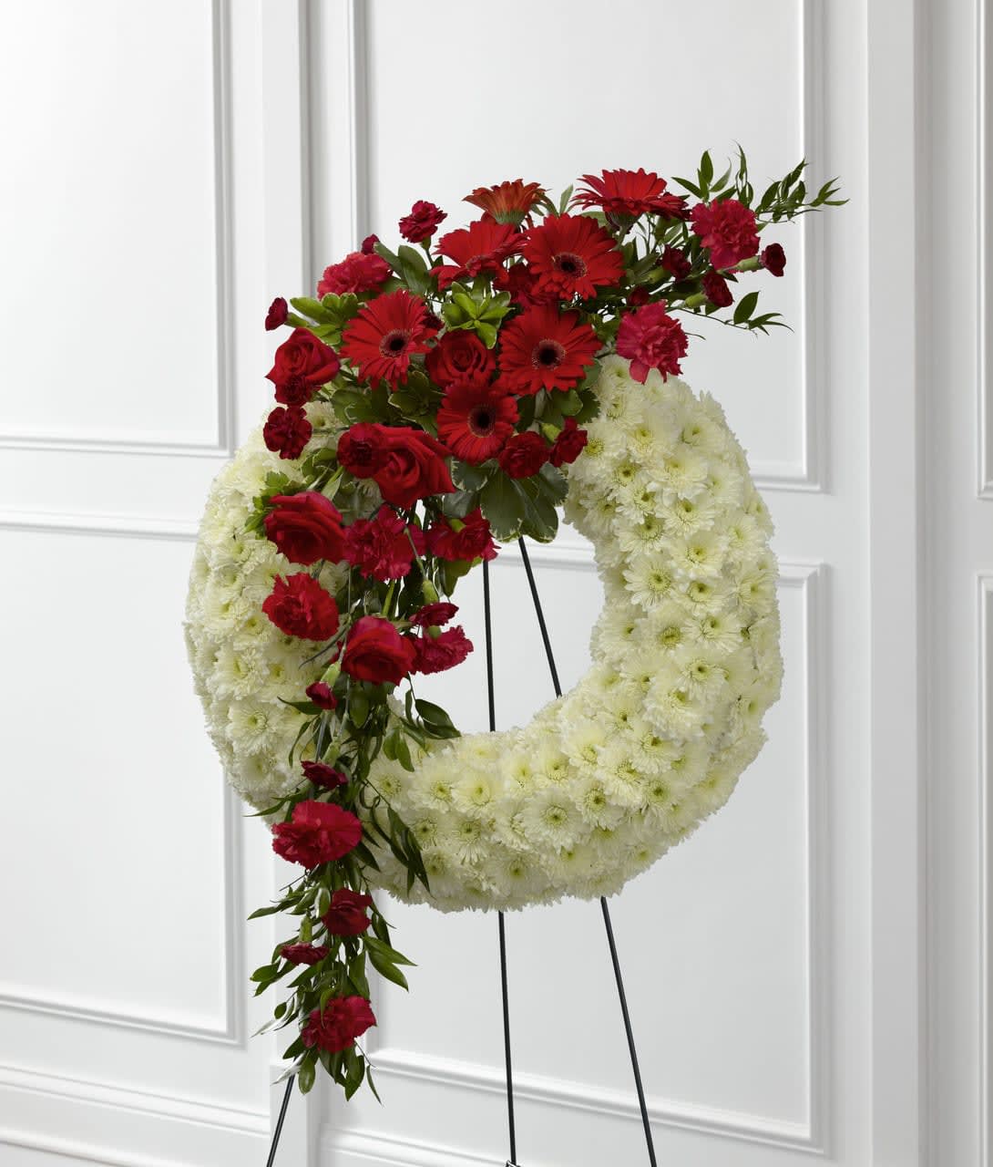 TLSP The Graceful Tribute Wreath - The Graceful Tribute Wreath creates a stunning presentation of love's serenity for their final farewell service. Red roses, carnations and gerbera daisies are accented with burgundy mini carnations and a variety of lush greens to create a sweeping arrangement that glides across the face of a snow white wreath consisting of chrysanthemums making this a remembrance for one who has touched your life like none other. Displayed on a wire easel. Approximately 58"H x 27"W.  Your purchase includes a complimentary personalized gift message. 