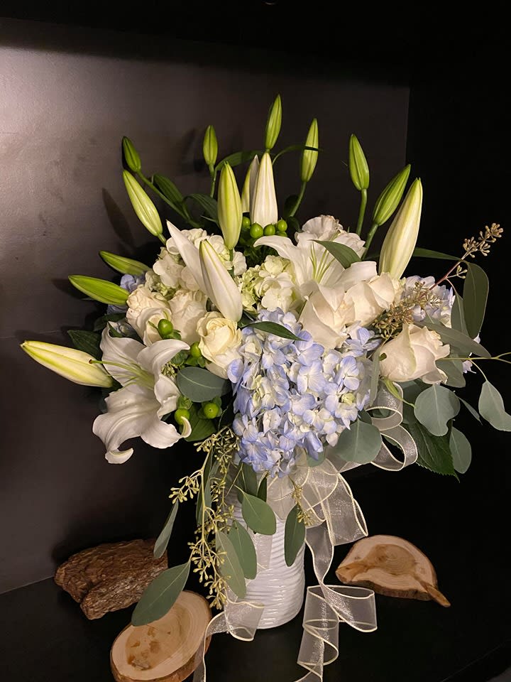 White lilies and pale blue hydrangeas in a white vase with ribbon