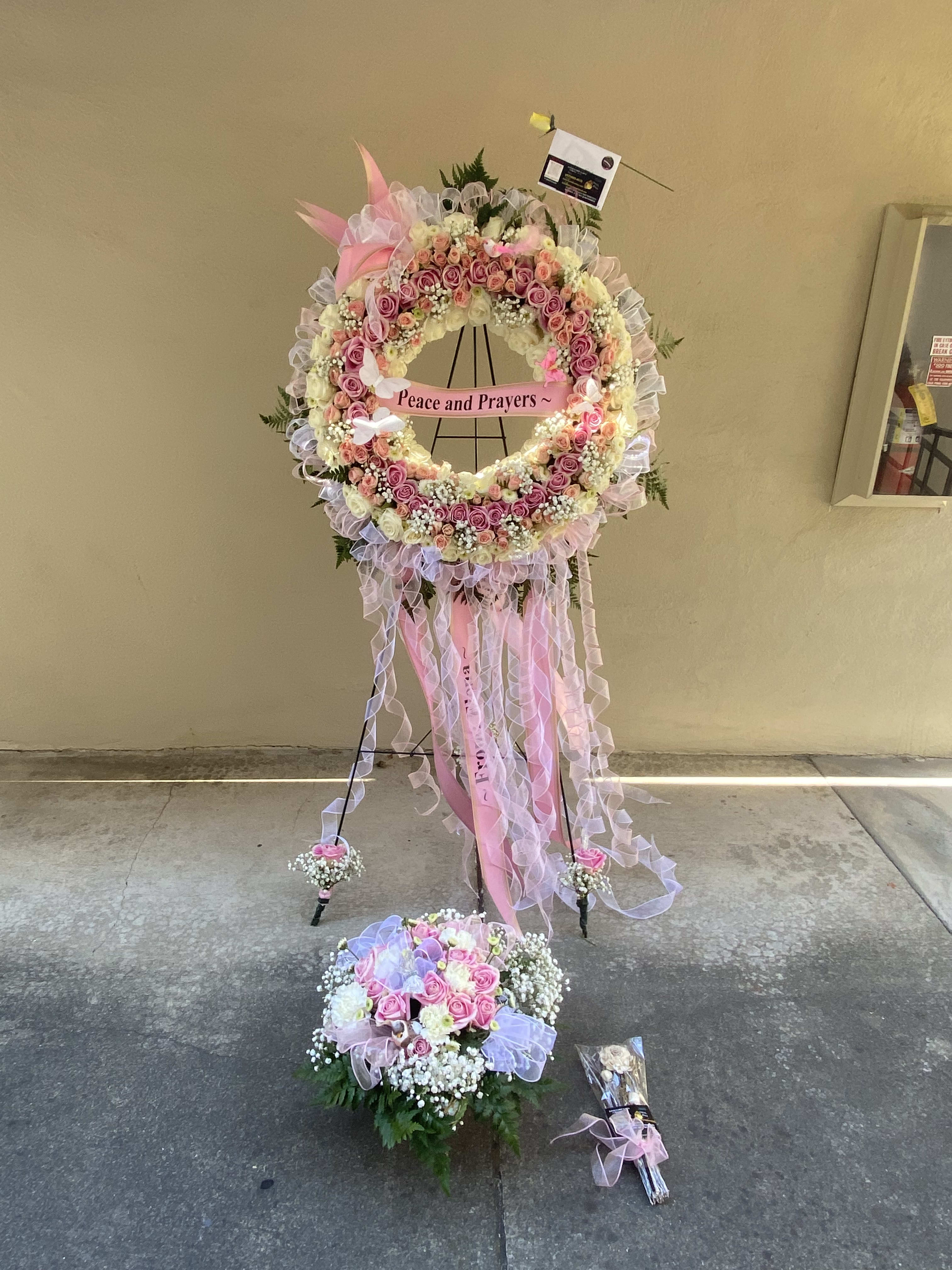 Pink and white floral standing wreath with ribbons and a "Peace and Prayers" sign