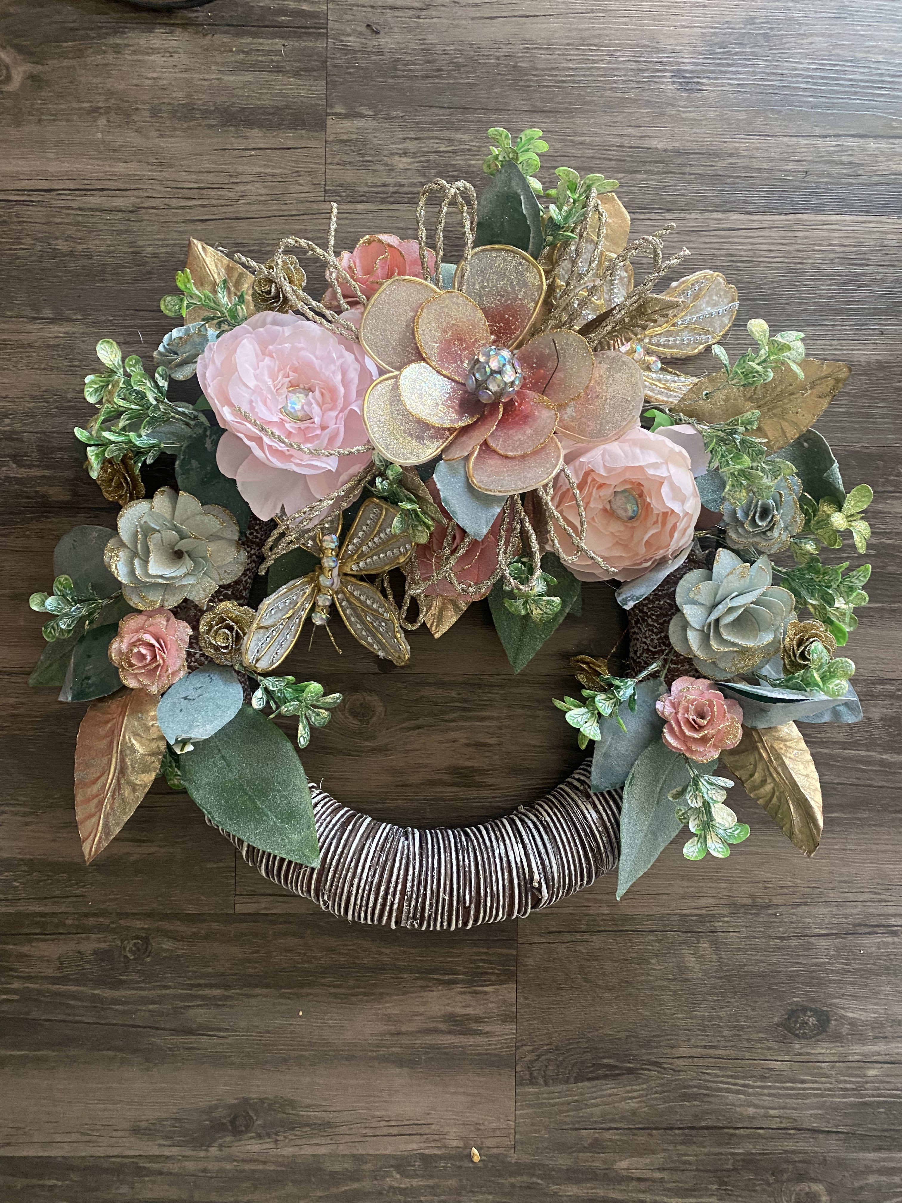 Decorative floral wreath with pink and gold flowers on a wrapped ring base