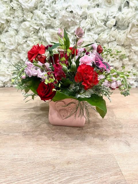 Red and pink mixed flower arrangement in a pink vase with a heart accent