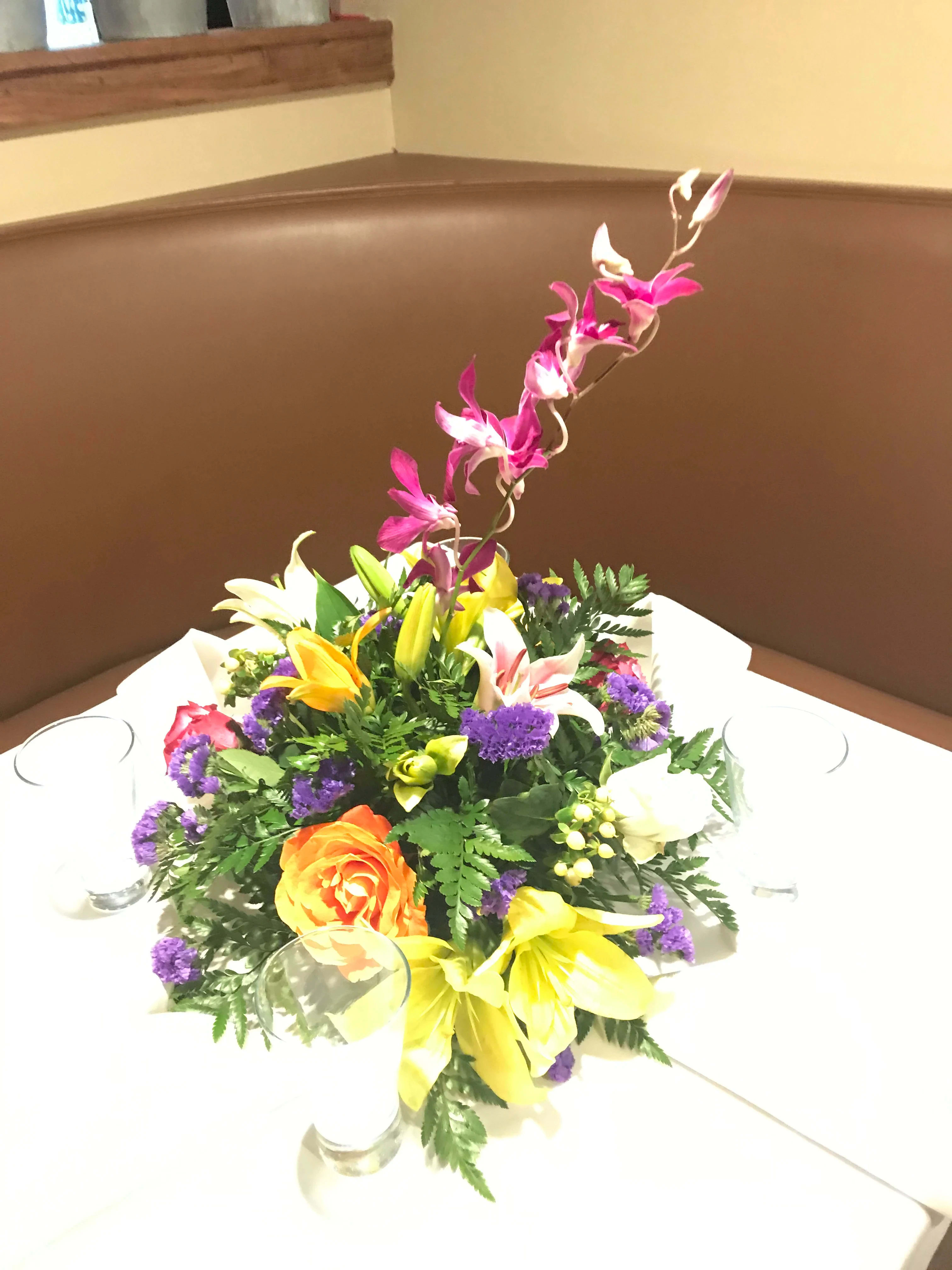 Colorful floral centerpiece in a low arrangement with a tall orchid stem