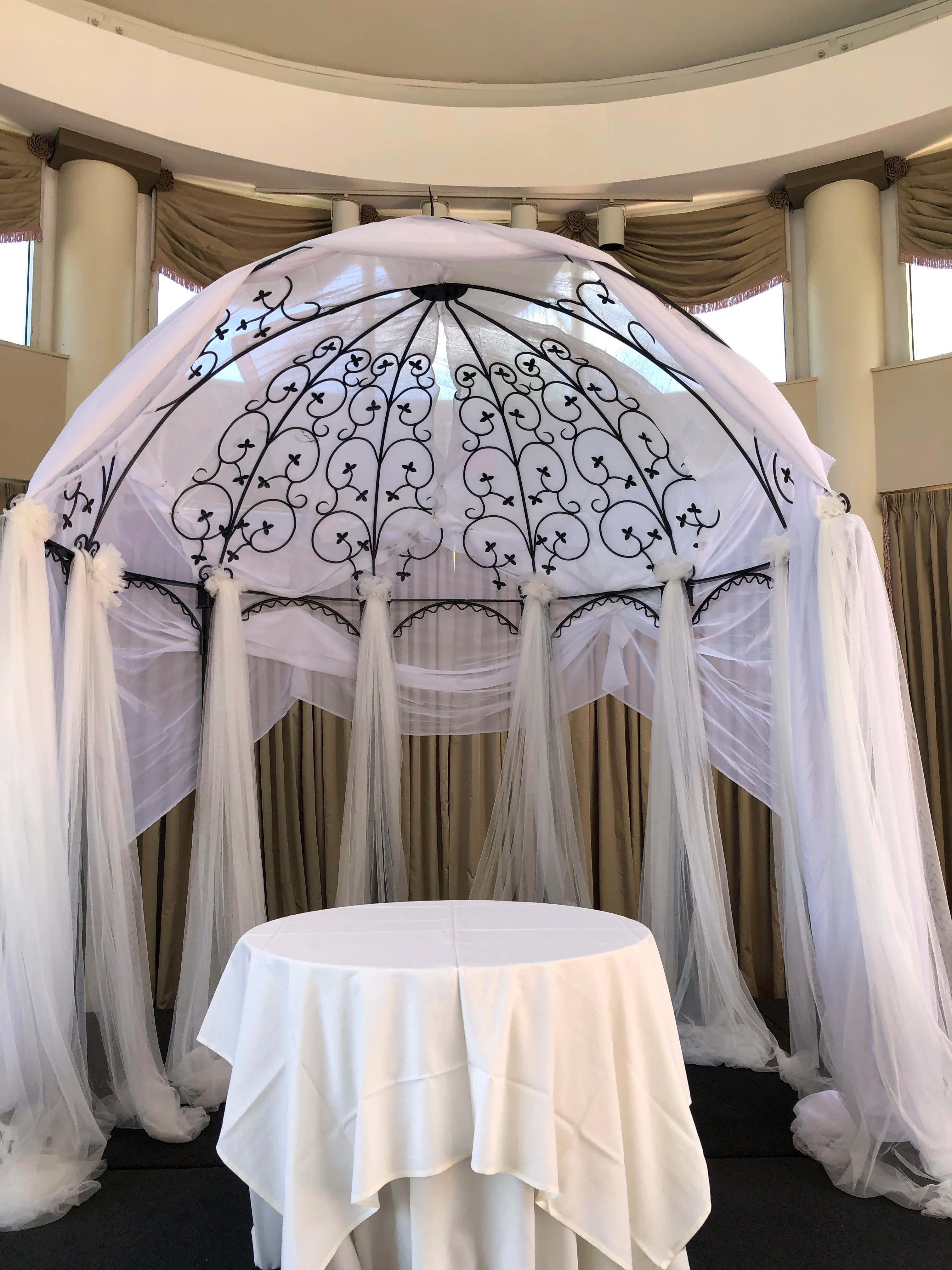 White draped wedding canopy with black scrollwork and a round table beneath