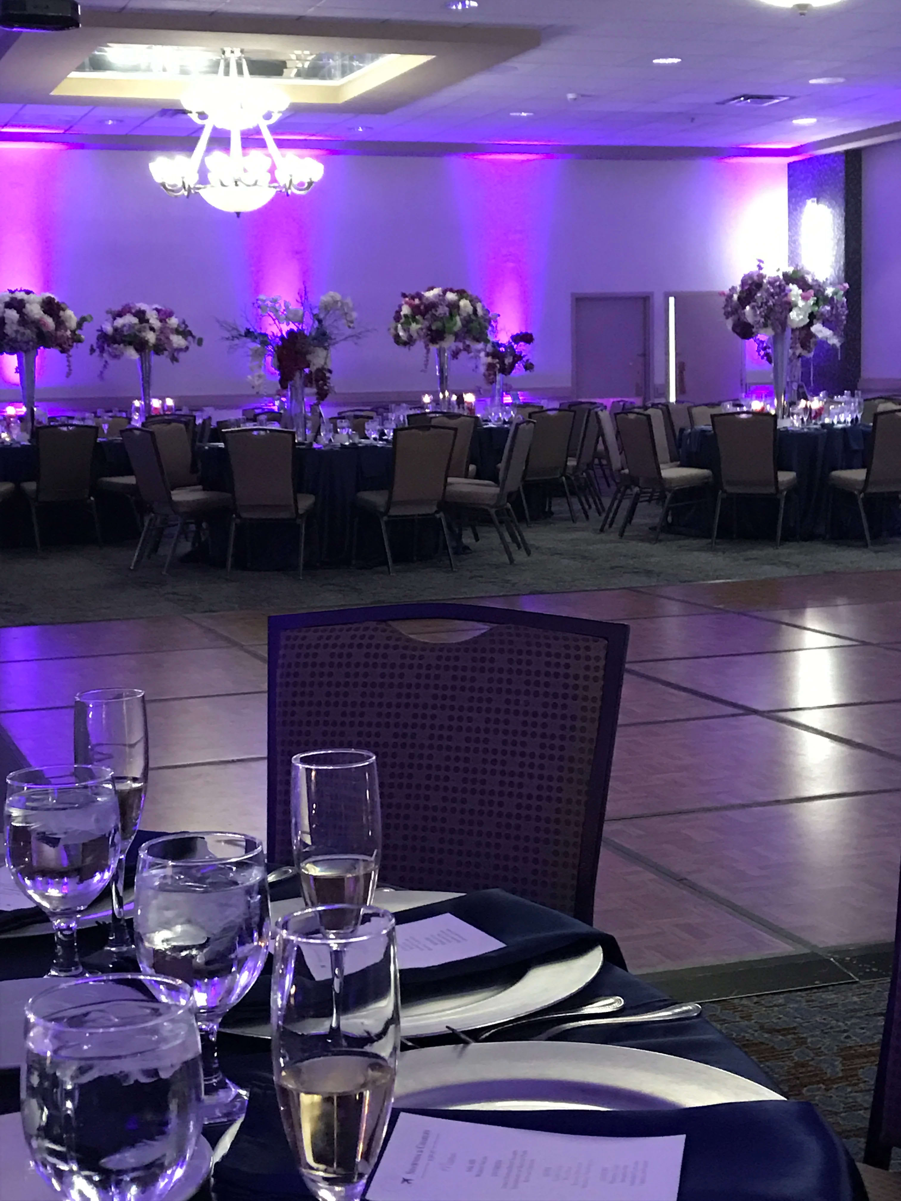 Banquet hall with tall floral centerpieces on round tables under purple lighting
