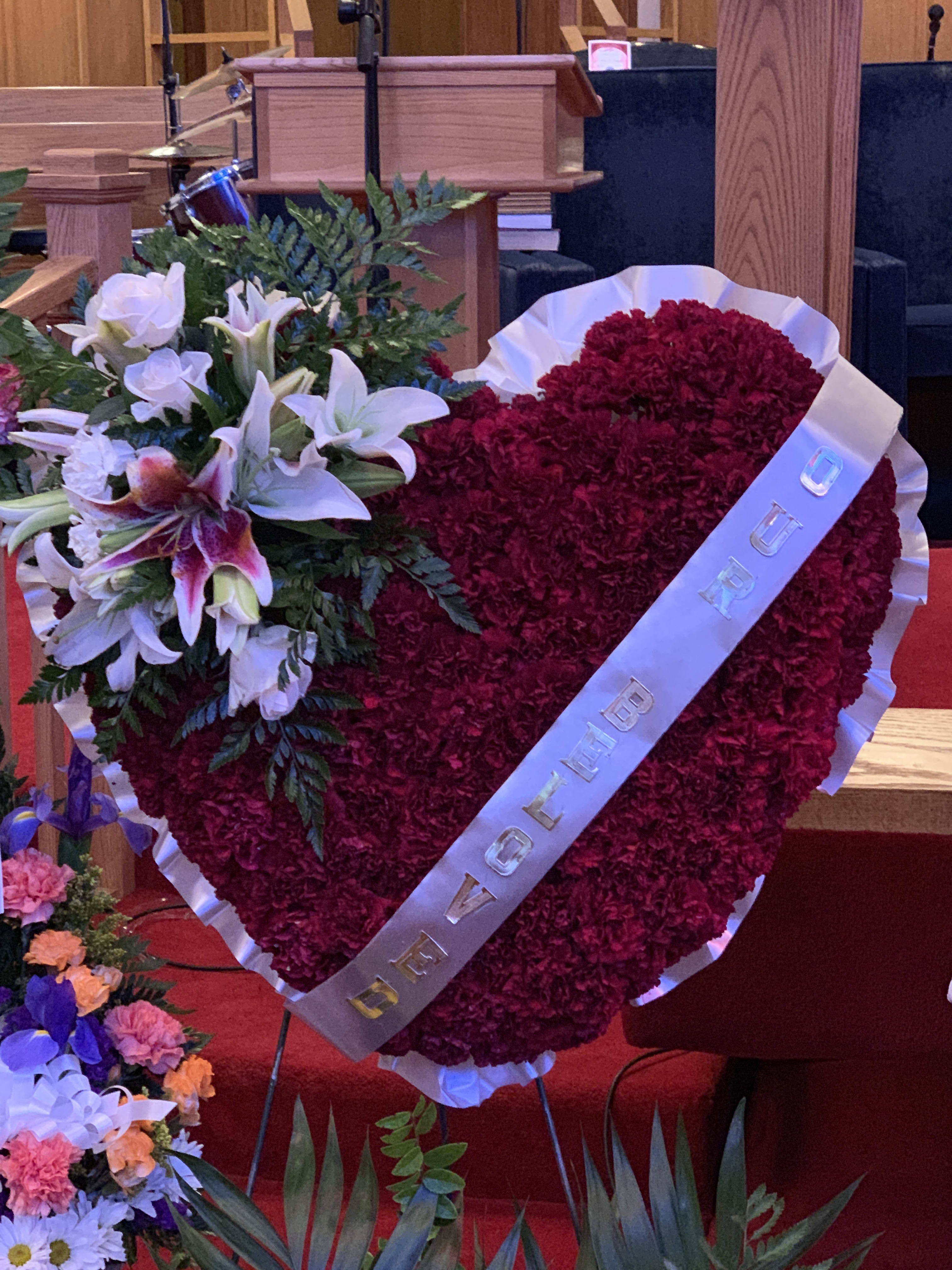 Heart-shaped red floral tribute with white lilies and a ribbon