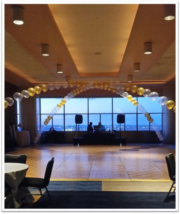 Balloon arch in gold, white, and clear balloons inside a banquet room