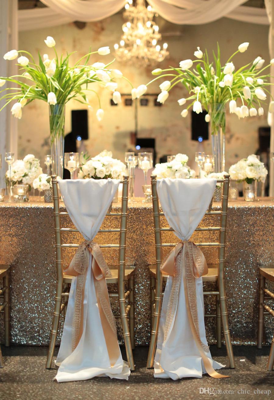 Tall white floral centerpieces on gold chairs at a decorated table