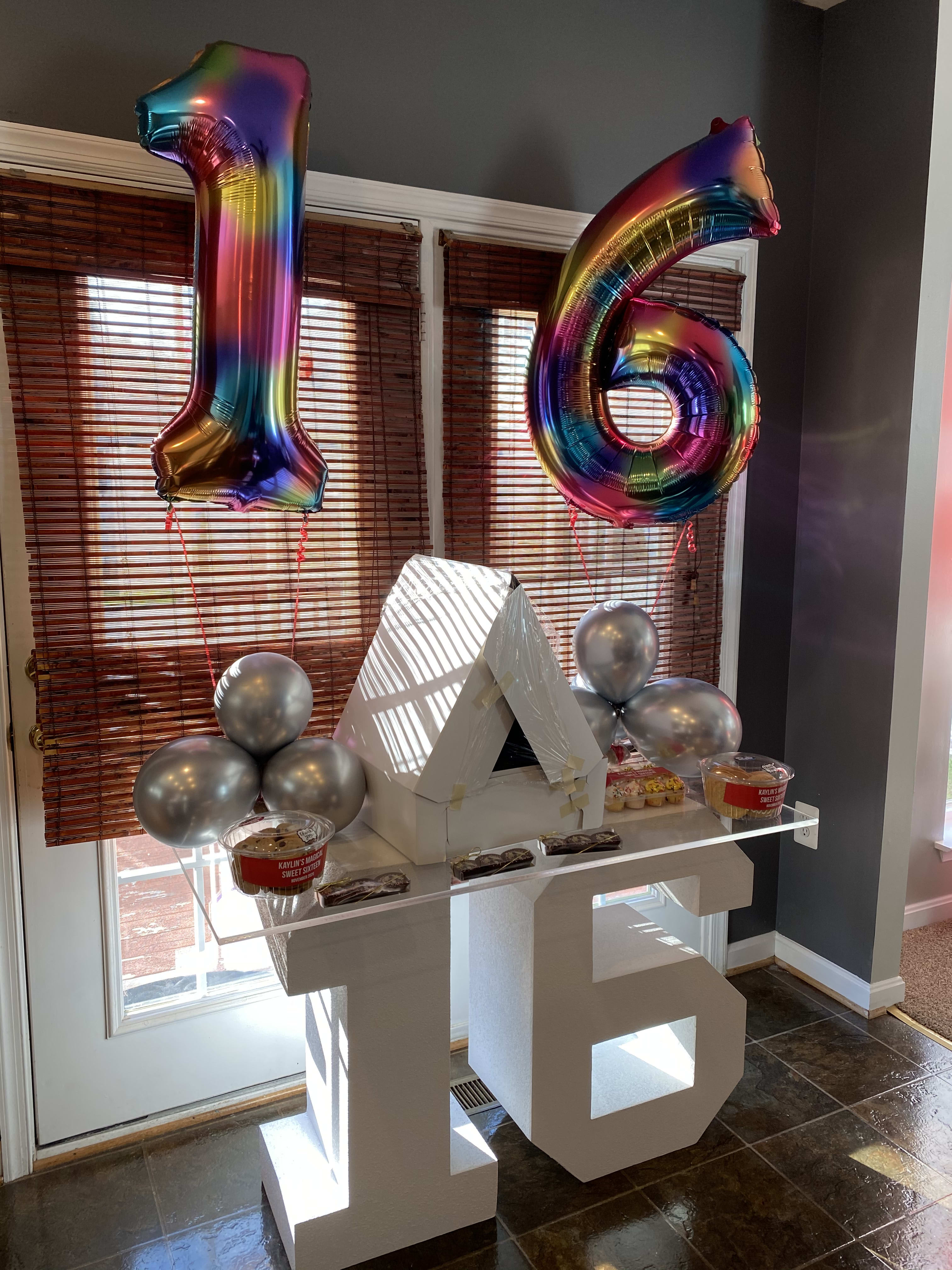 Rainbow balloons shaped like 1 and 6 above a decorated table