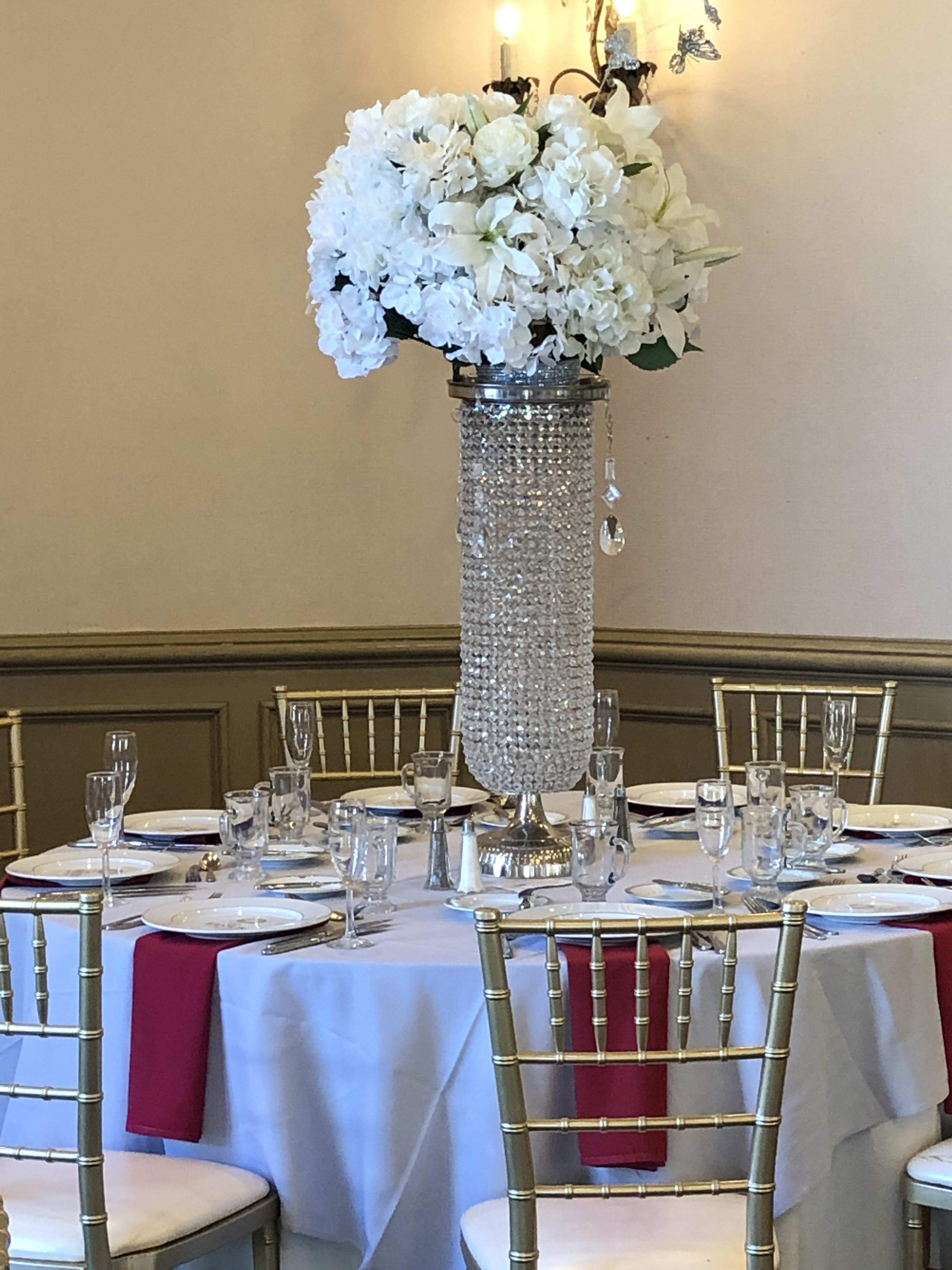 White floral centerpiece on a tall crystal-covered stand