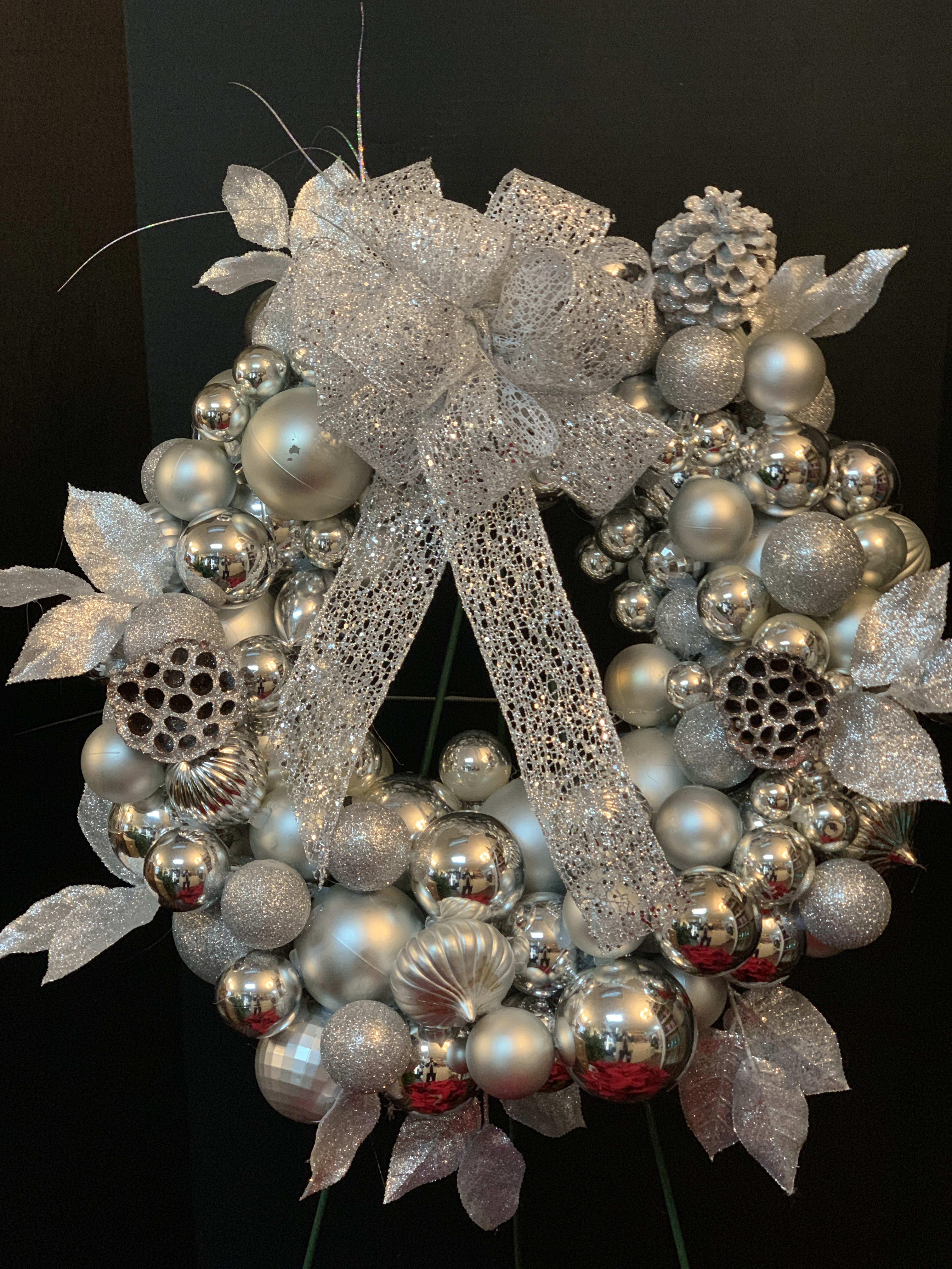 Silver decorative wreath with glittery ornaments and a large mesh bow
