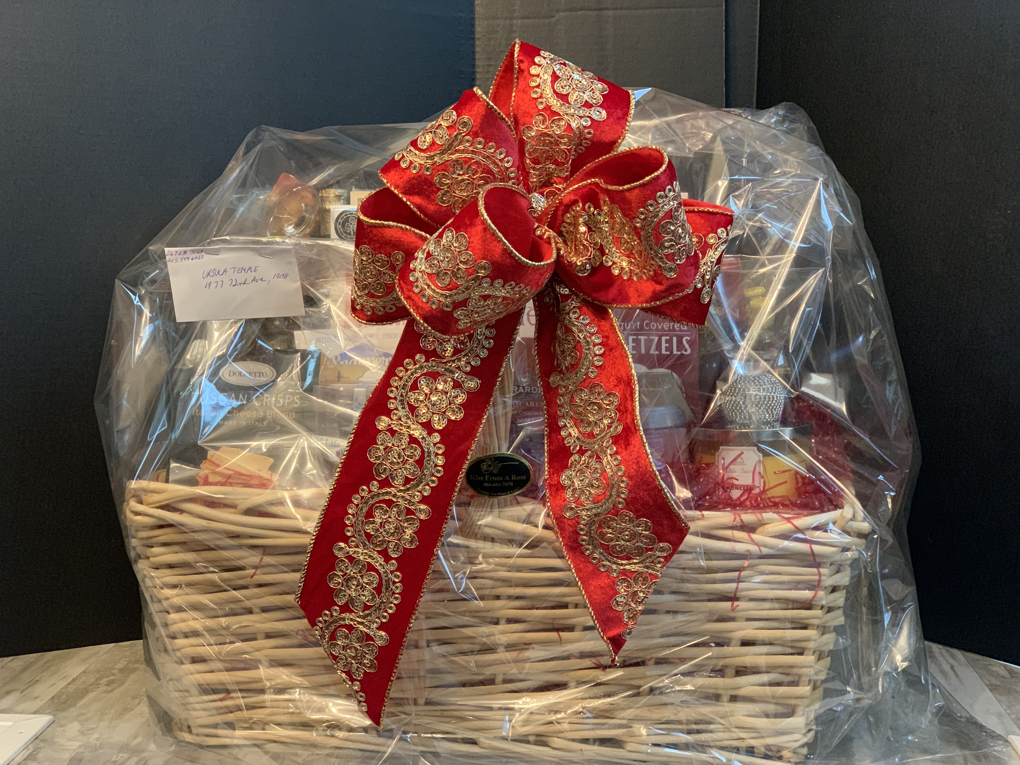 Gift basket wrapped in clear plastic with a large red decorative bow