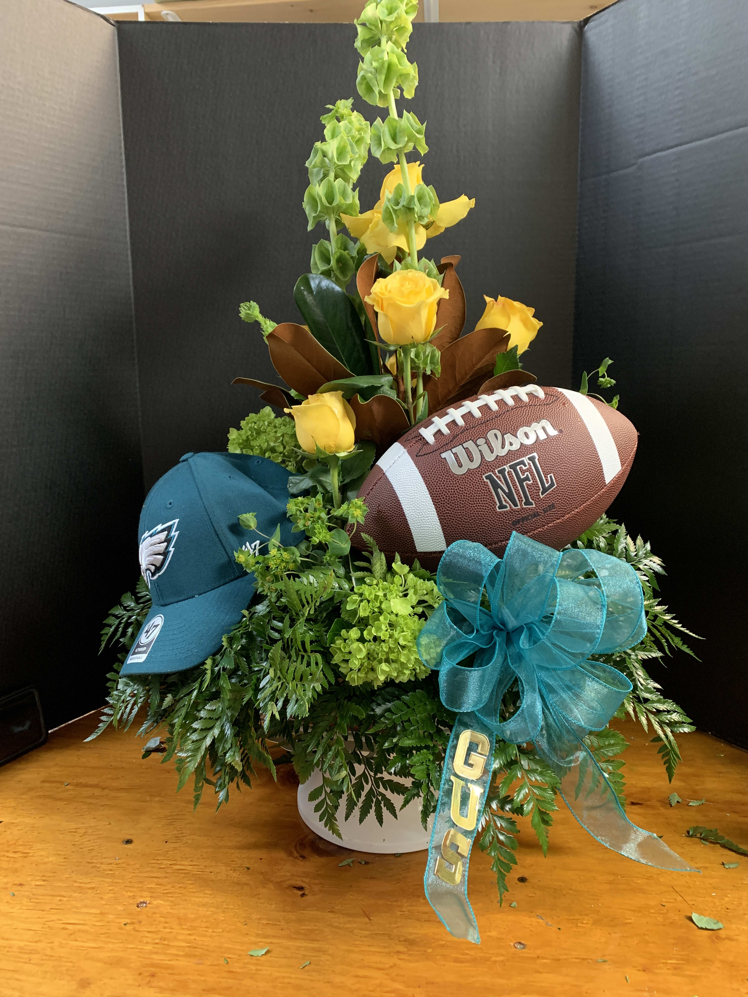 Yellow roses arranged with a football, cap, and teal ribbon in a white container