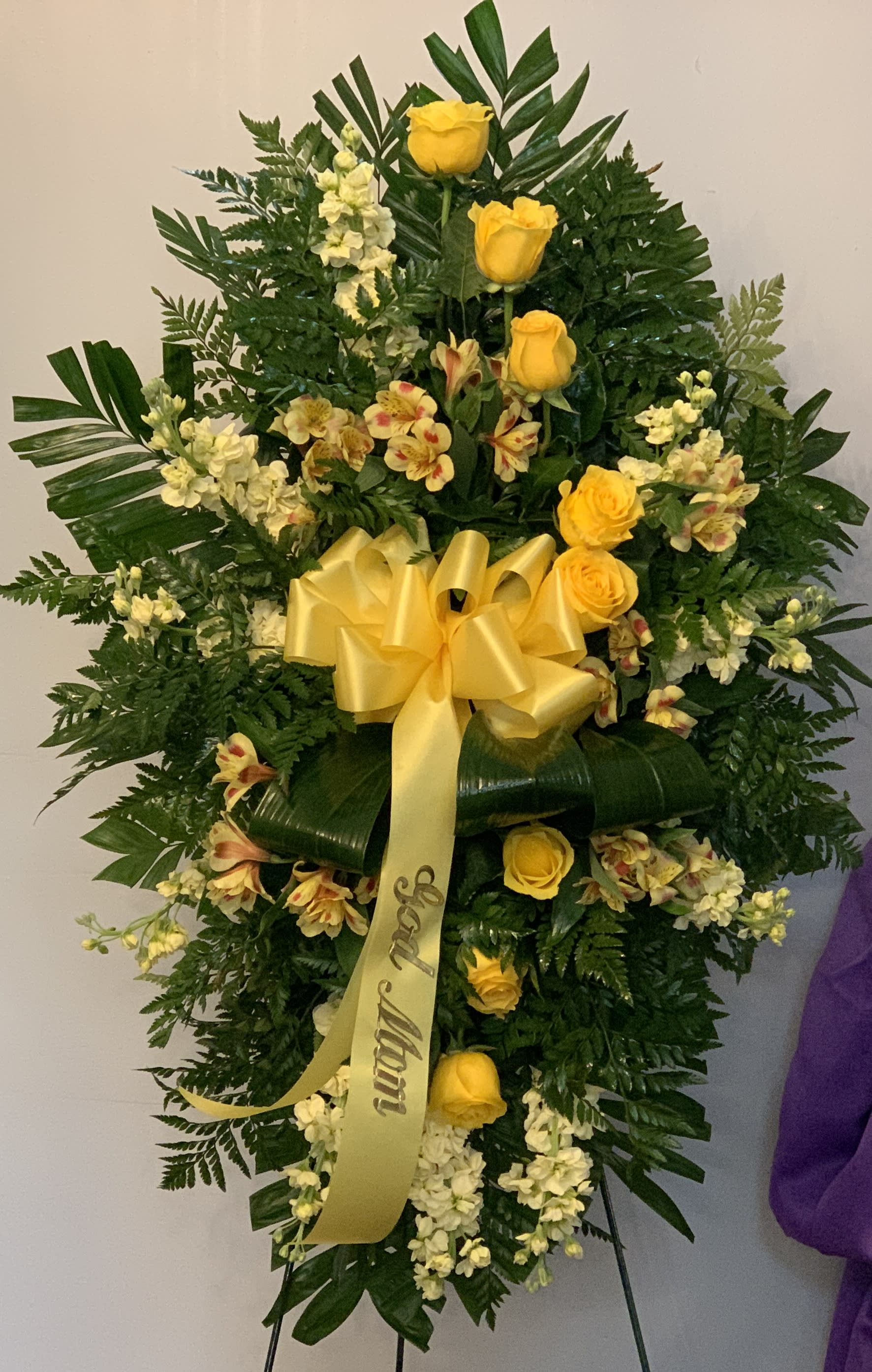 Standing floral spray with yellow roses and white blooms on a ribboned easel