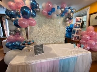 Pink, blue, and silver balloon decorations around a draped table