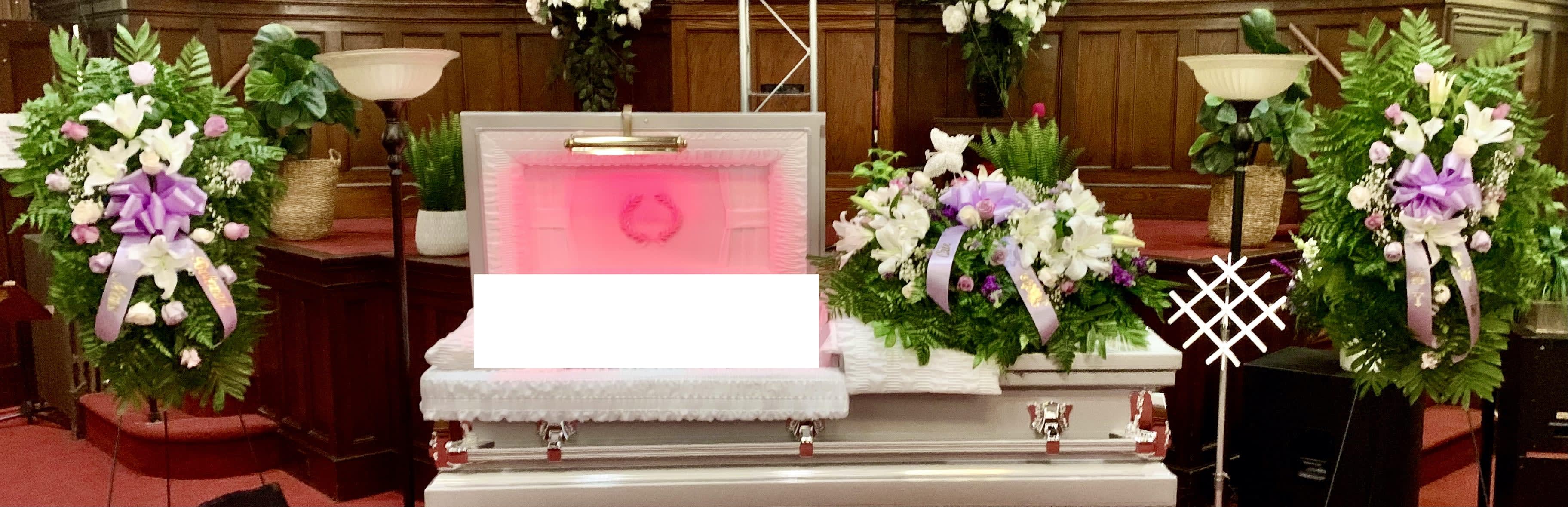 White casket surrounded by purple and white funeral flower sprays