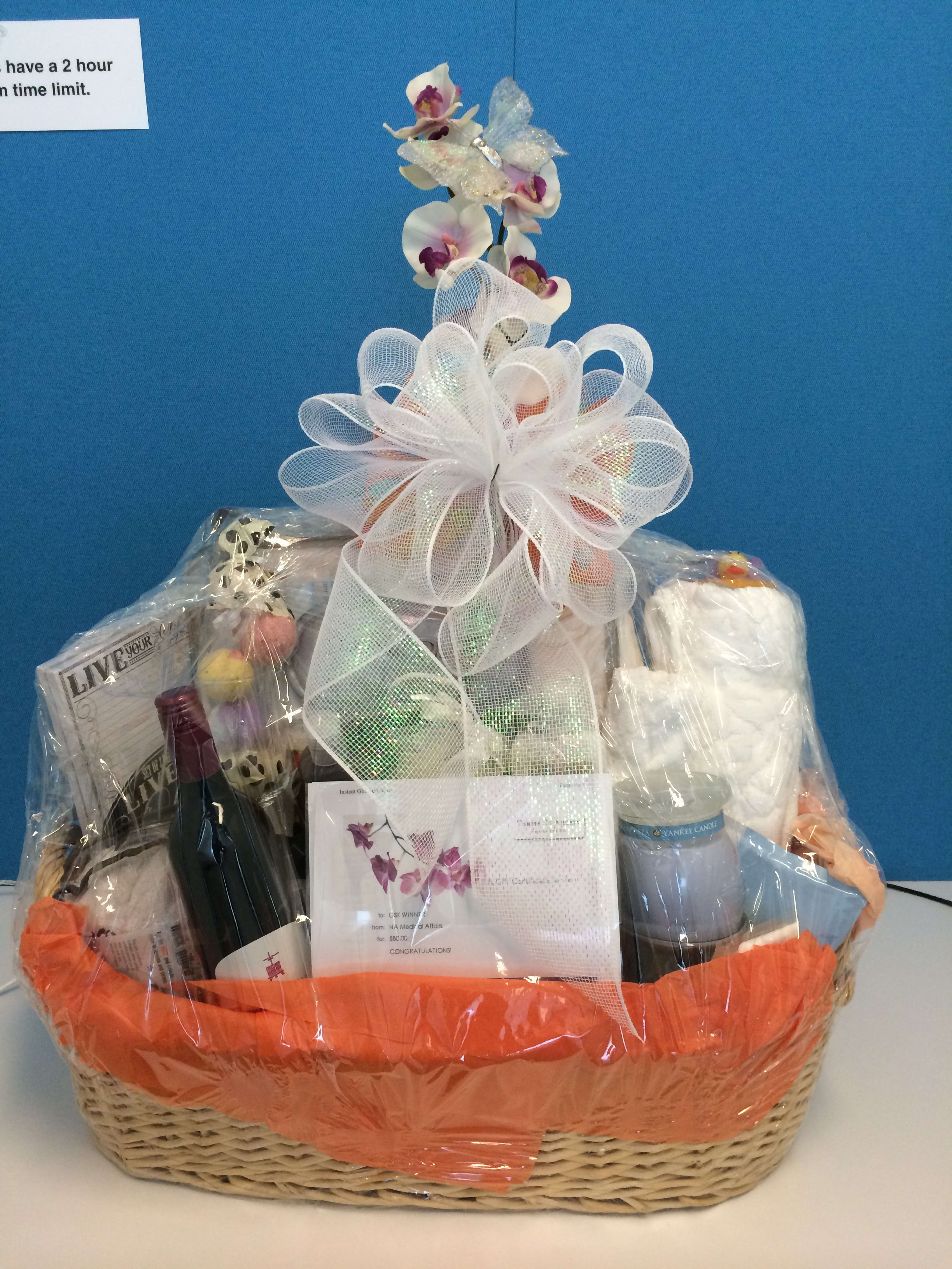 Gift basket with orchids, wine, a candle, and assorted items wrapped in cellophane