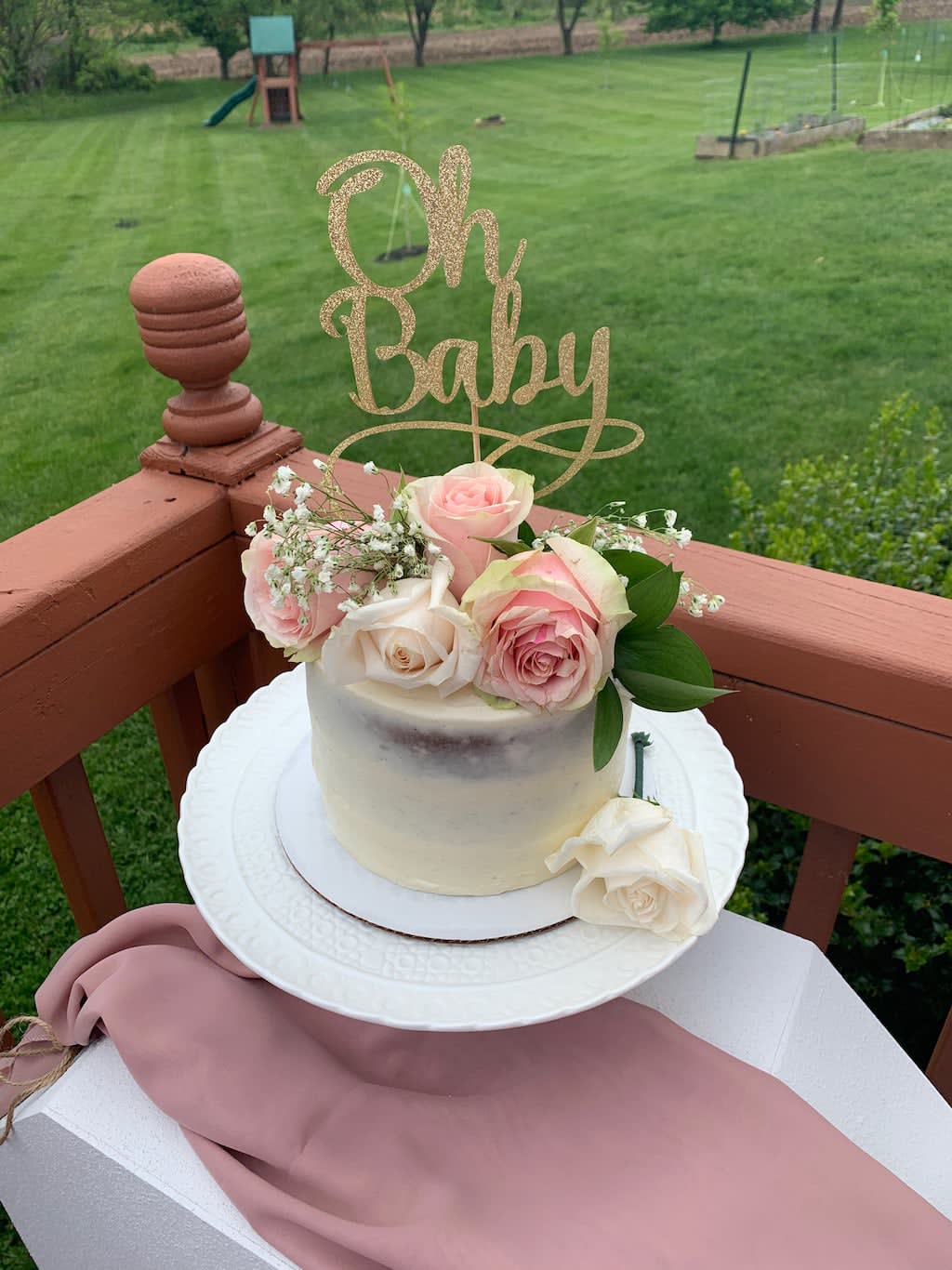 Small cake topped with pink and white roses and a glittery "Oh Baby" sign
