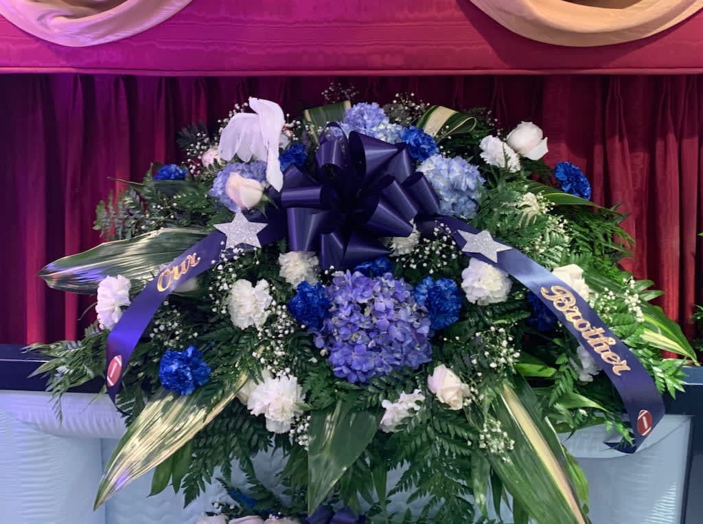 Large blue and white funeral spray with ribbons and a bow