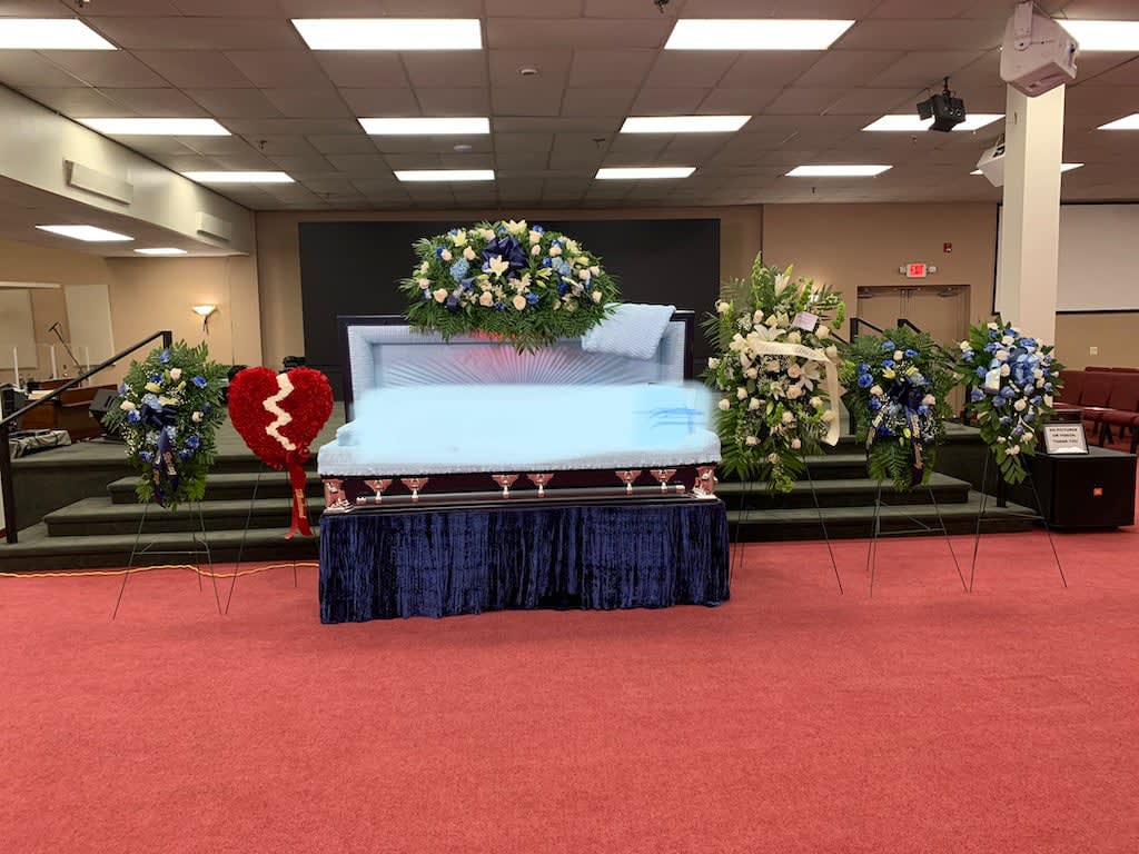 Casket surrounded by blue and white funeral flower sprays