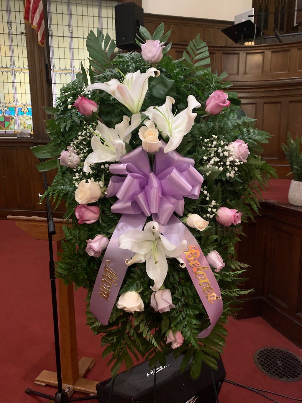 Large funeral wreath with white lilies, pink roses, and a purple ribbon bow