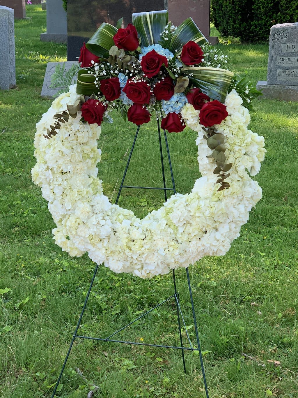 Standing funeral wreath with white flowers and red roses on an easel