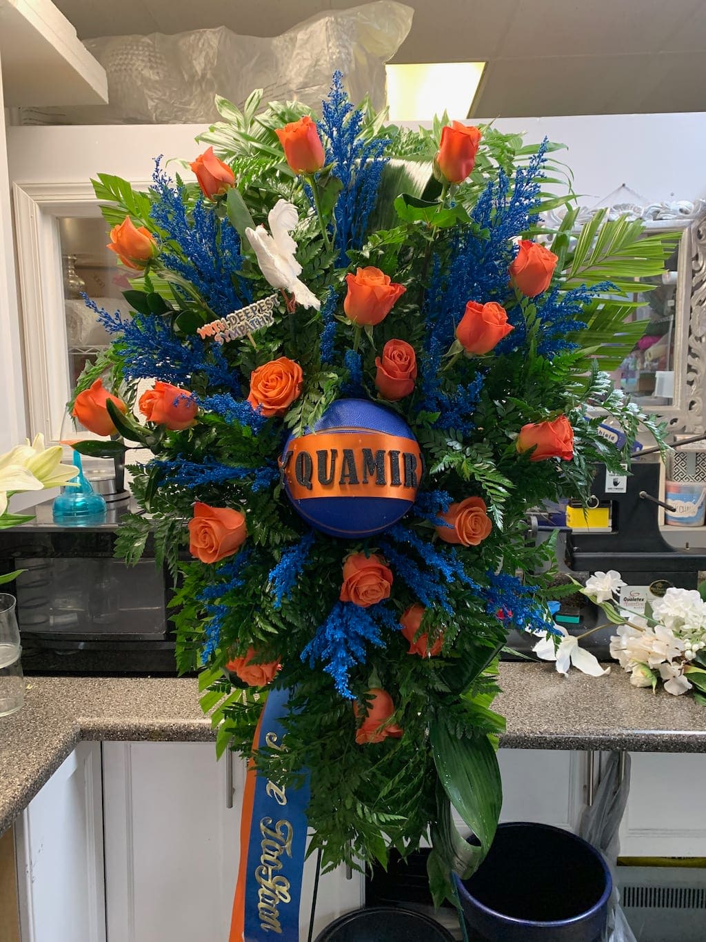 Large orange rose funeral spray with blue accents and a memorial ribbon
