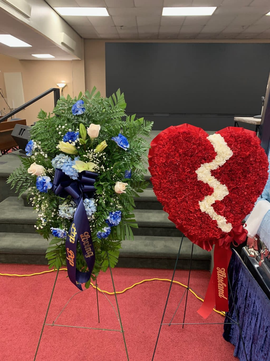 Two standing floral funeral sprays, one heart-shaped red wreath with a white crack