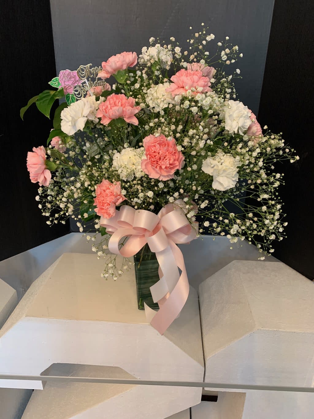 Pink and white carnations with baby's breath in a vase, tied with a pink ribbon
