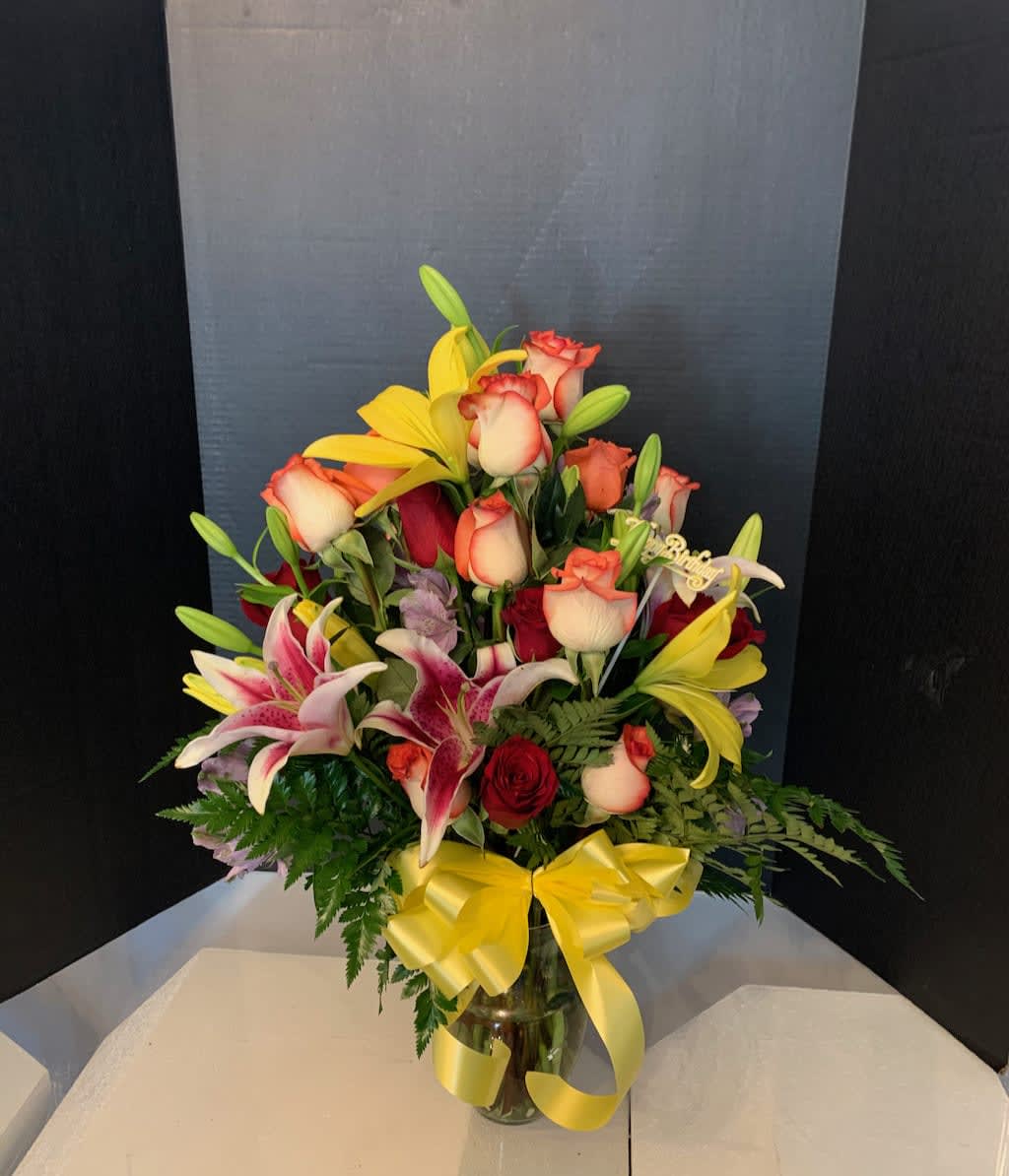 Mixed bouquet of roses and lilies in a glass vase with a yellow ribbon