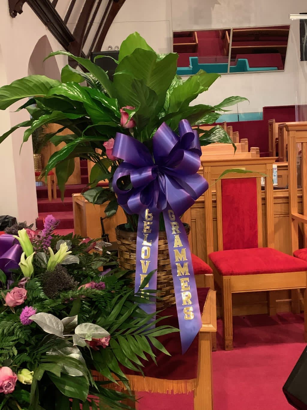 Large green plant arrangement with a purple ribbon in a church pew