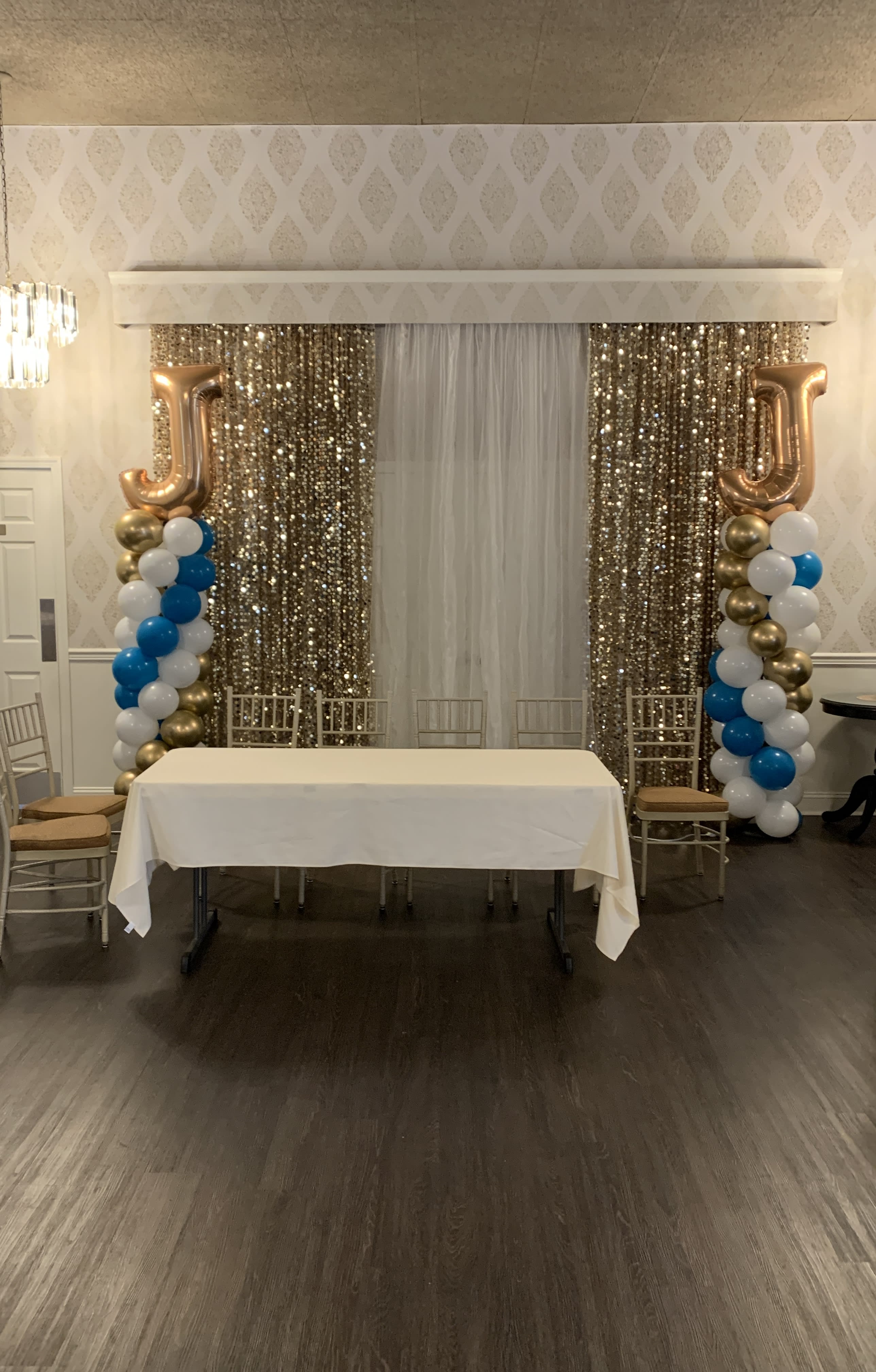 Event backdrop with gold sequin curtains, balloon columns, and a table