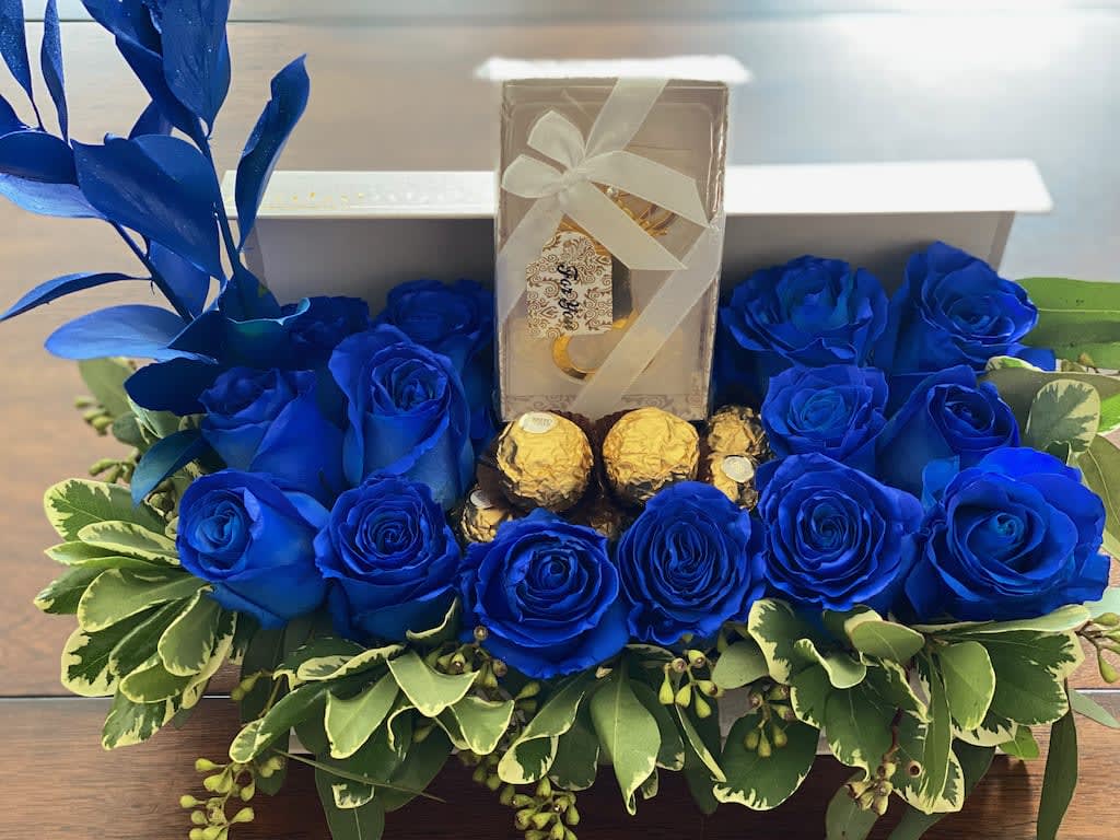 Blue roses arranged around a gift box and chocolates