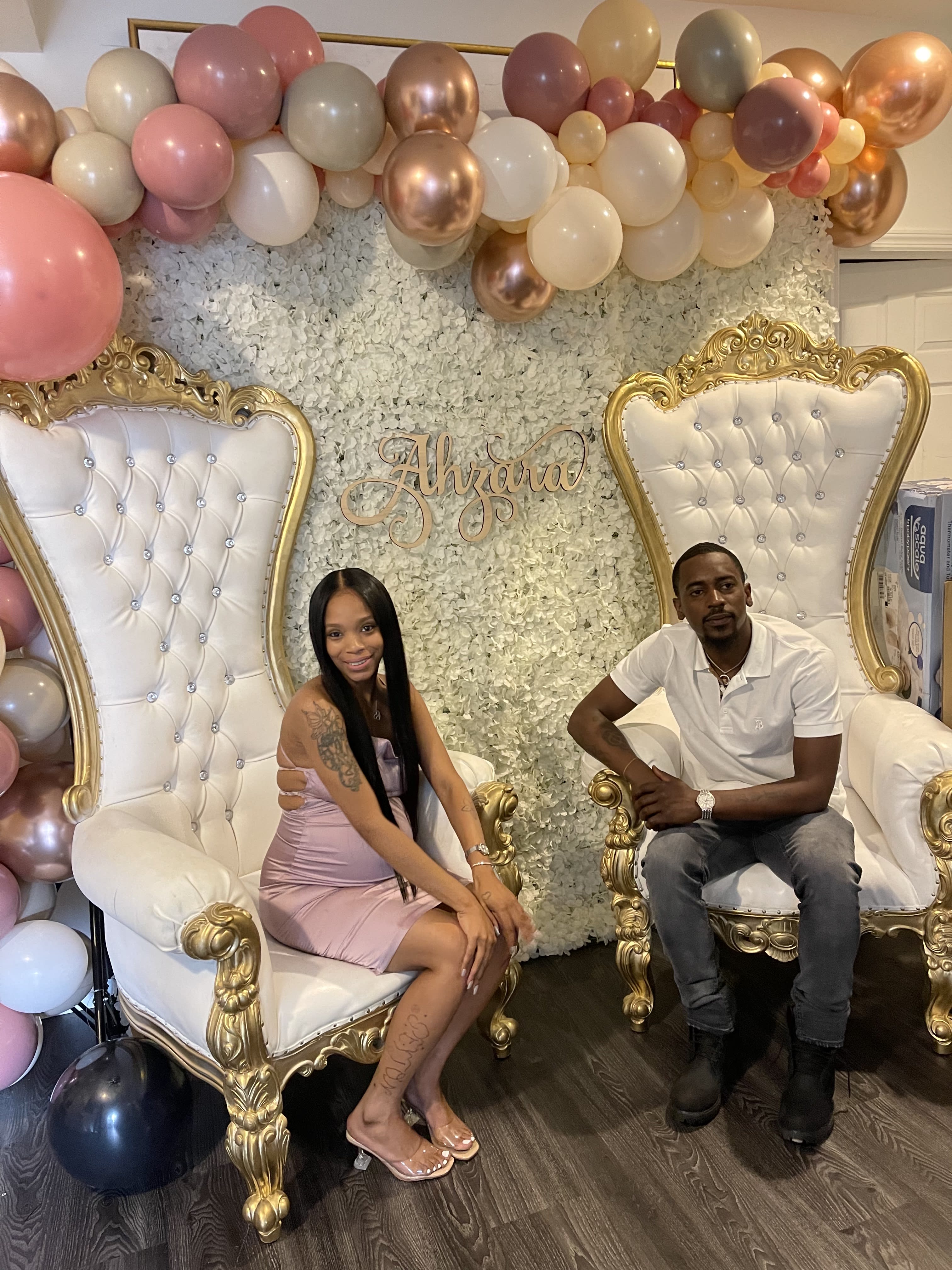 Balloon backdrop with two ornate white-and-gold chairs and seated couple